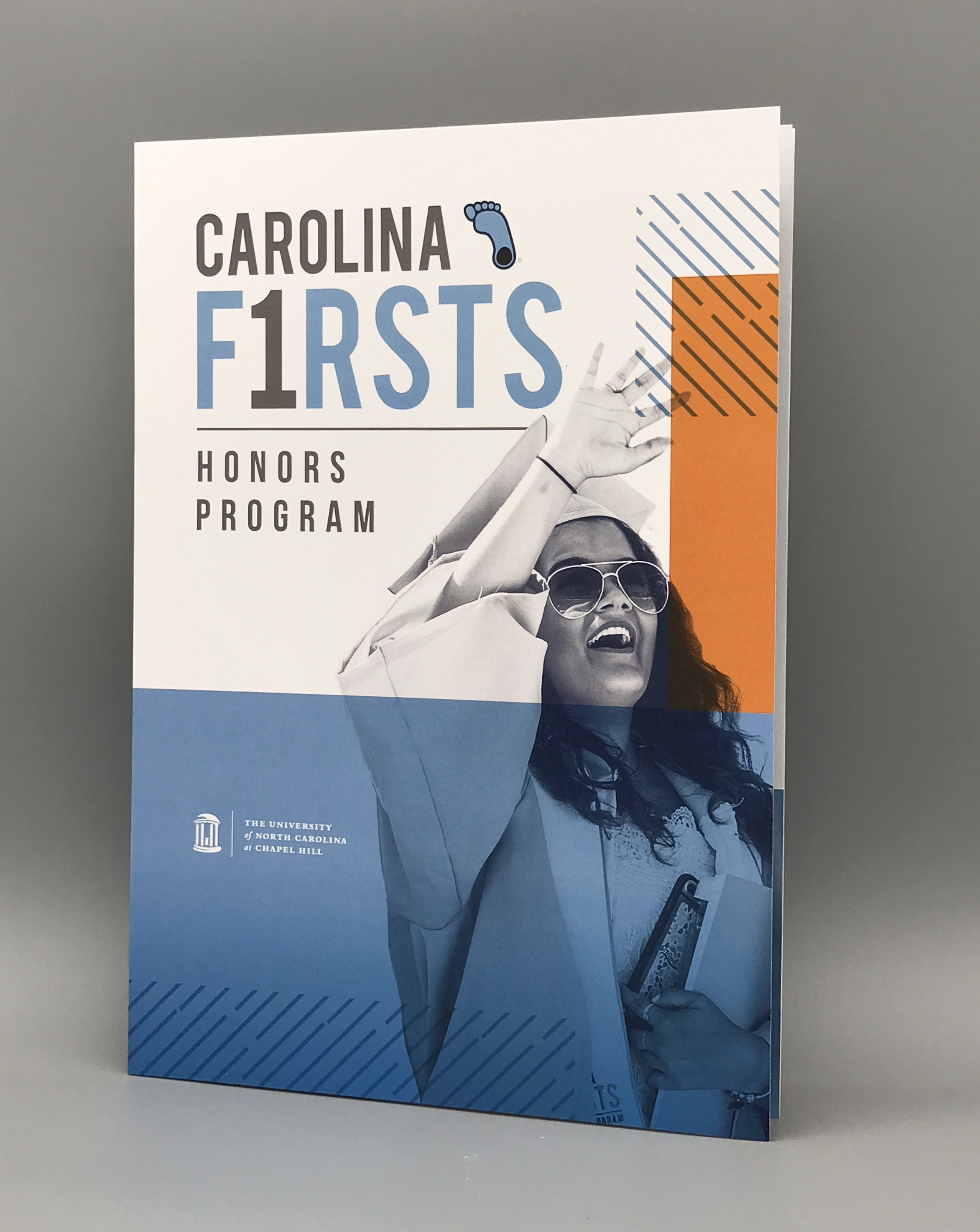Photograph of the Carolina Firsts booklet, featuring the Carolina Firsts logo and black and white photo of a female graduate wearing her commencement robe.